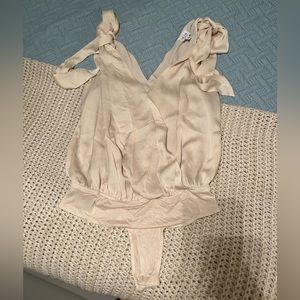 Small, cream-colored Lelis brand body suit with tied sleeves.